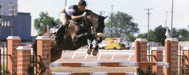 A rider in equestrian gear jumping over an obstacle with his horse